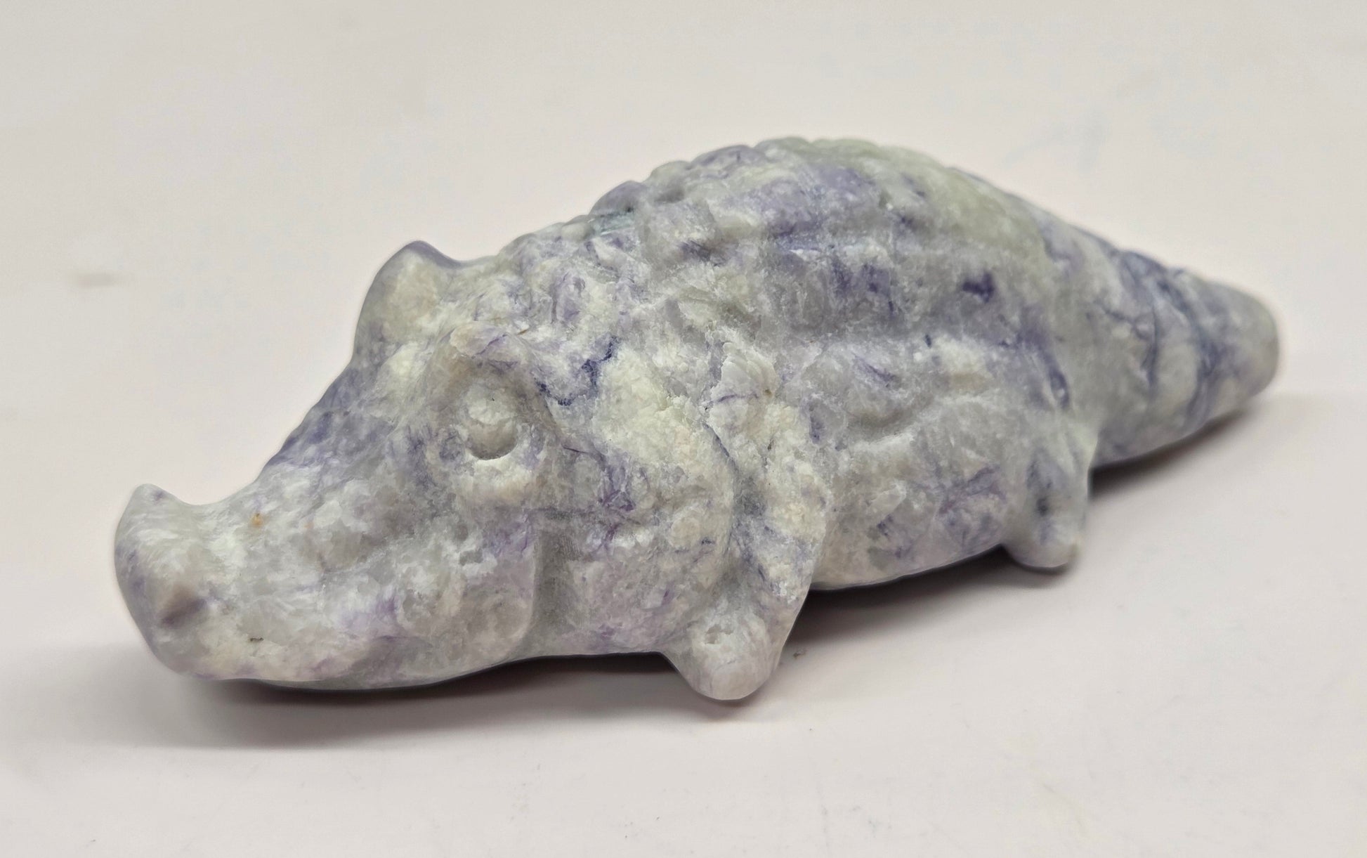 Carved lavender jasper crocodile on a white background