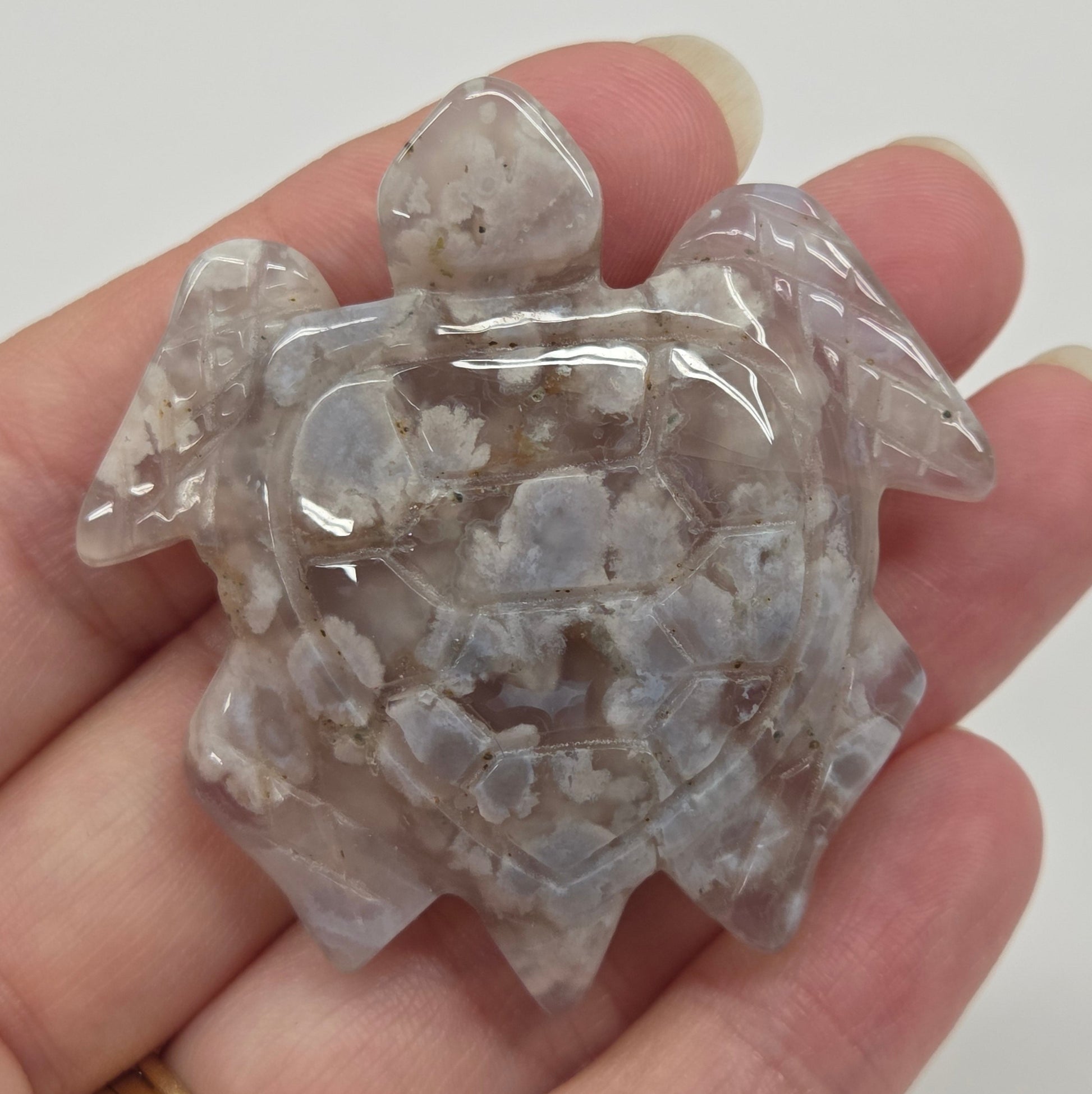 Hand holding a flower agate crystal turtle carving against a white background