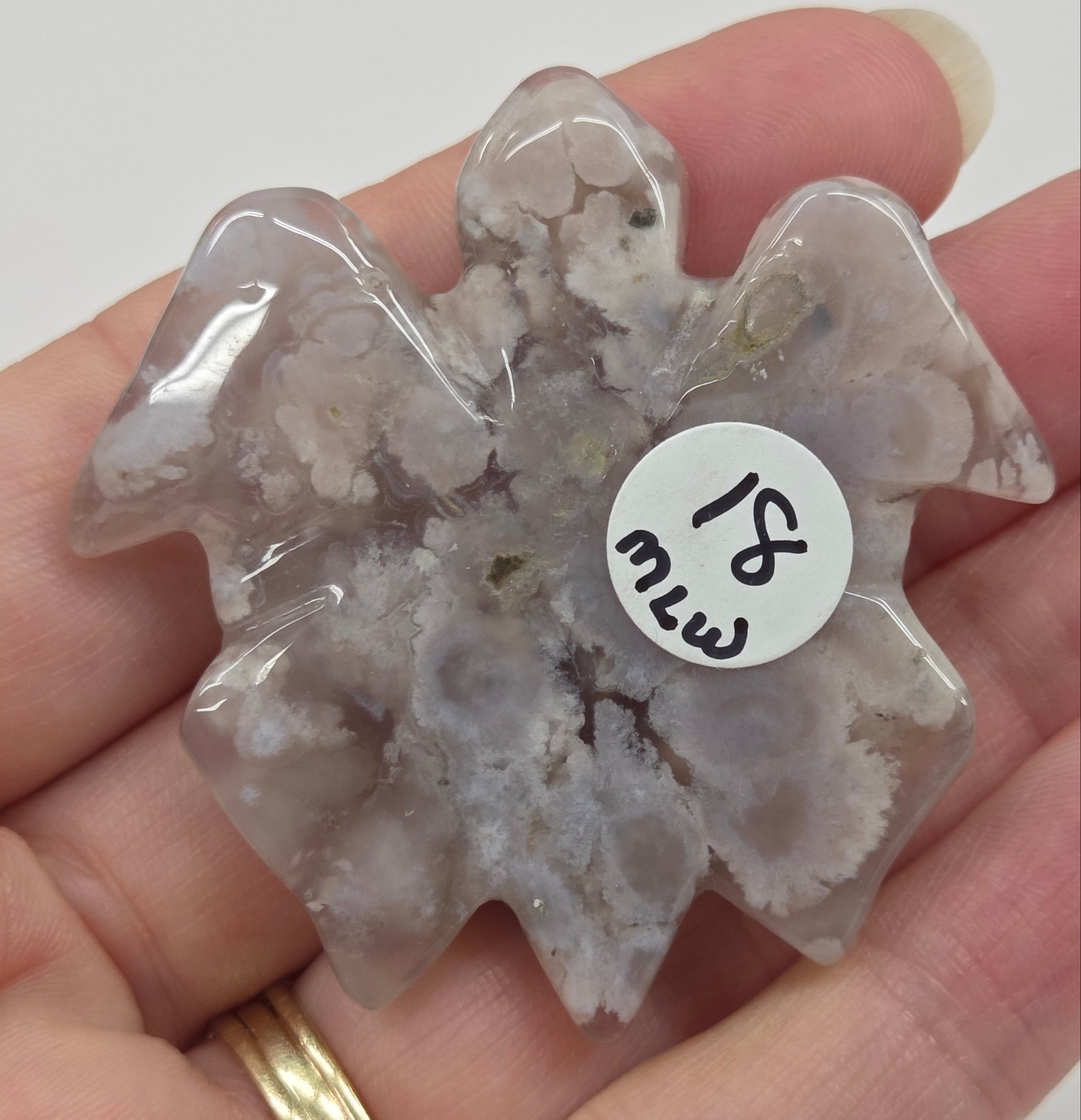 Hand holding a flower agate crystal turtle carving against a white background