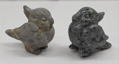 Two small bird carvings in different materials on a white surface