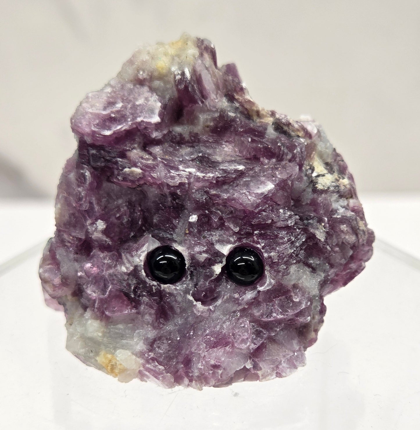 Purple Mica crystal with black eye  stones  and a carved smile on a white background