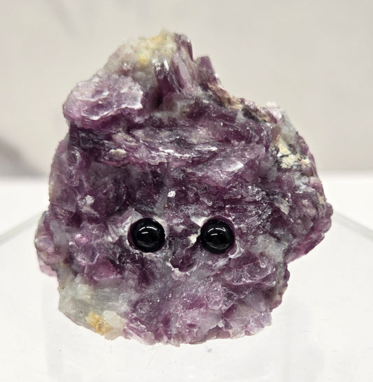 Purple Mica crystal with black eye  stones  and a carved smile on a white background