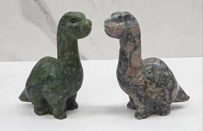 Two stone dinosaur figurines on a white surface with a light gray background