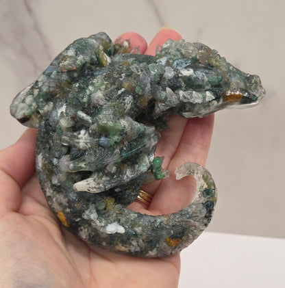 Hand holding resin with crystal chip carving of a dragon on a white background