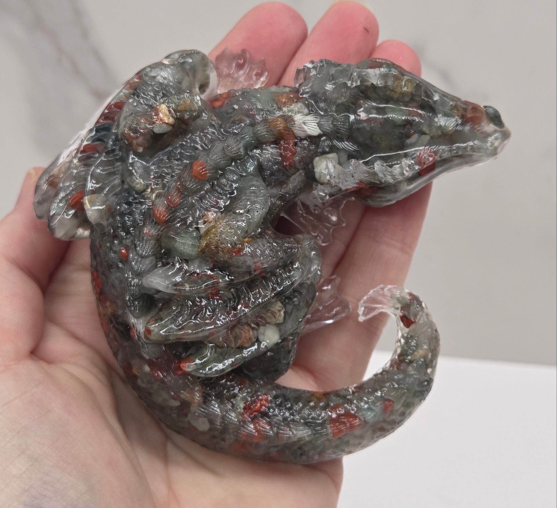 Hand holding resin with crystal chip carving of a dragon on a white background