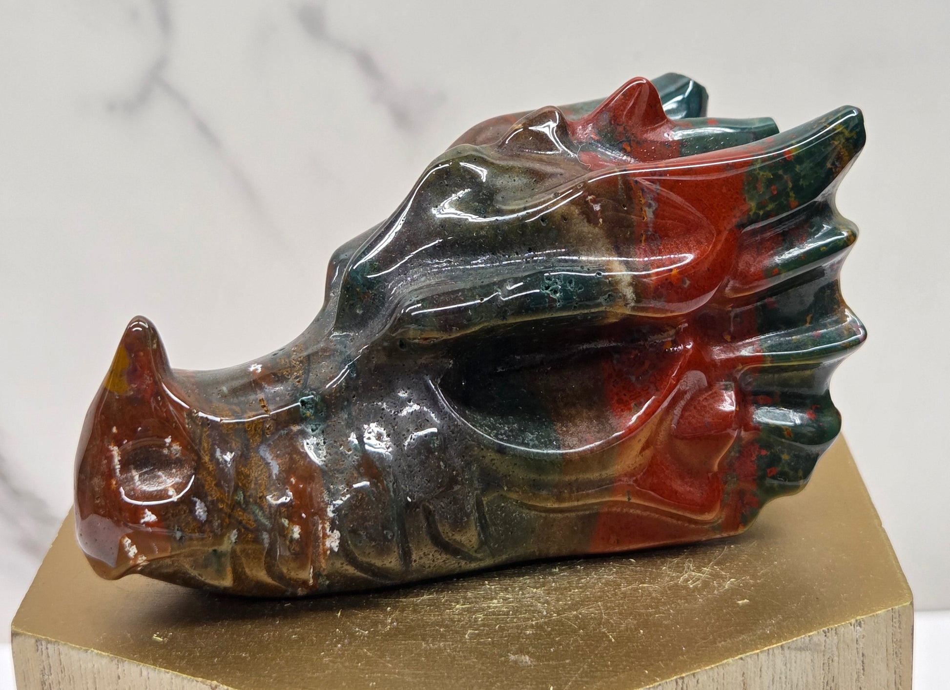 Decorative dragon head stone carving on a wooden stand with a plain background