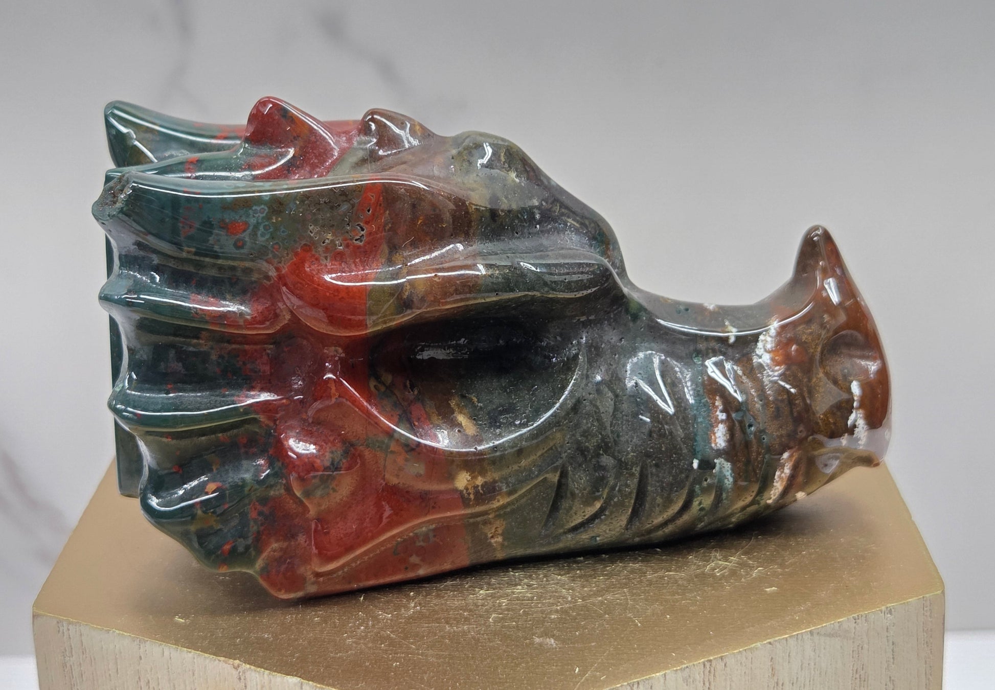 Decorative dragon head stone carving on a wooden stand with a plain background