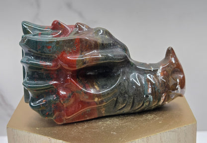 Decorative dragon head stone carving on a wooden stand with a plain background