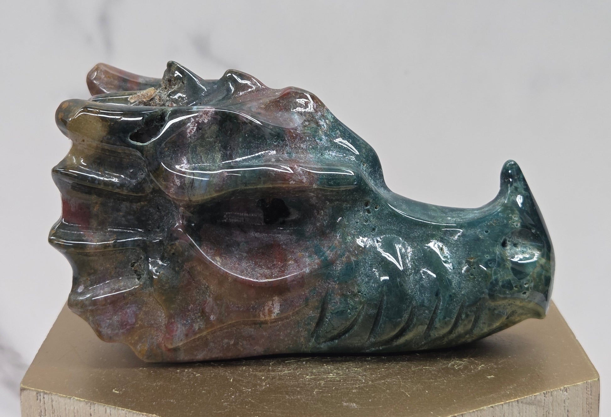 Decorative dragon head stone carving on a wooden stand with a plain background