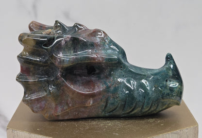 Decorative dragon head stone carving on a wooden stand with a plain background