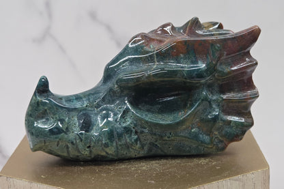 Decorative dragon head stone carving on a wooden stand with a plain background