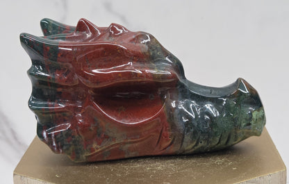 Decorative dragon head stone carving on a wooden stand with a plain background