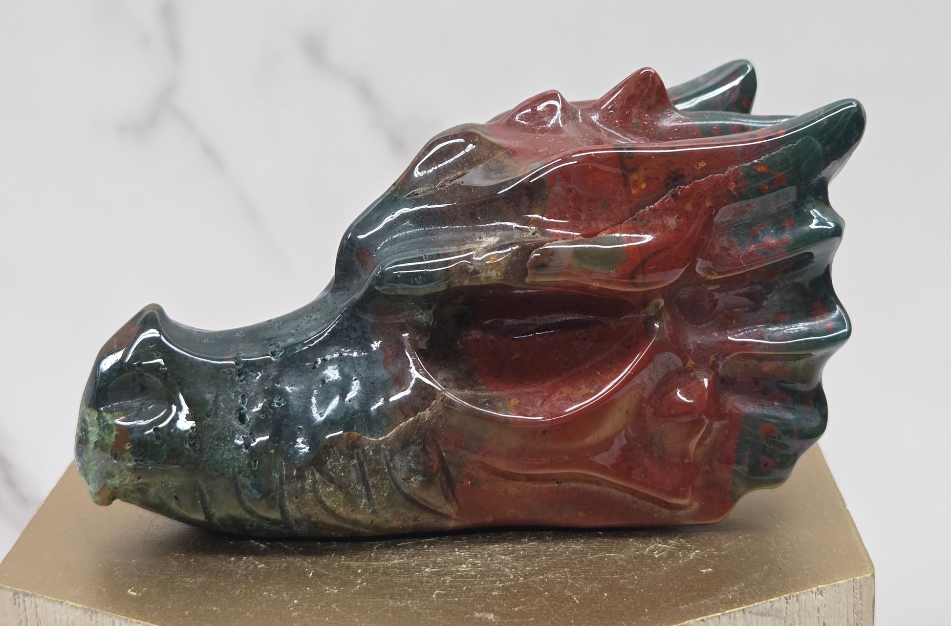 Decorative dragon head stone carving on a wooden stand with a plain background
