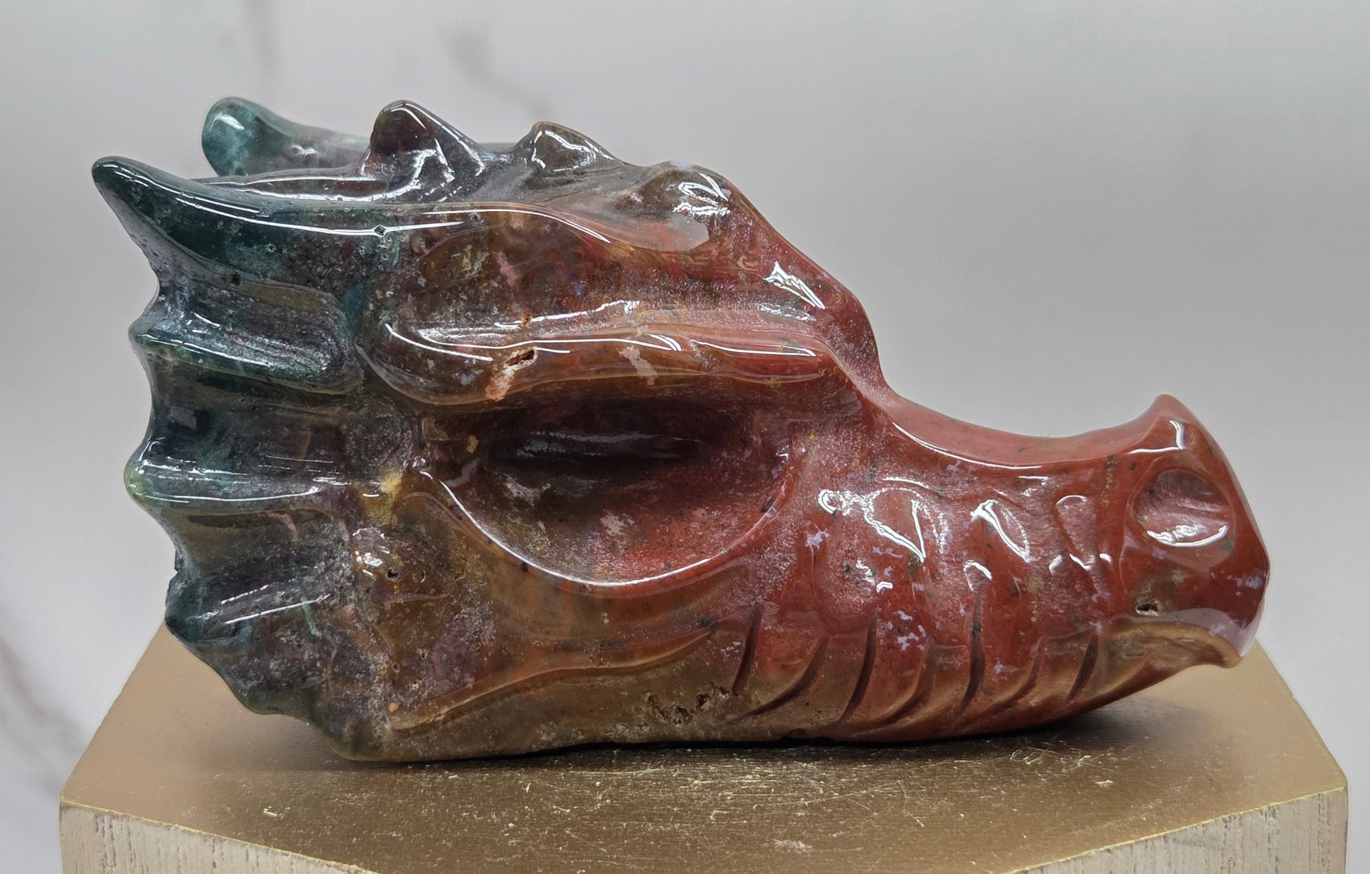 Decorative dragon head stone carving on a wooden stand with a plain background