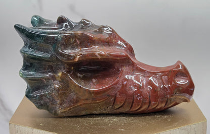 Decorative dragon head stone carving on a wooden stand with a plain background