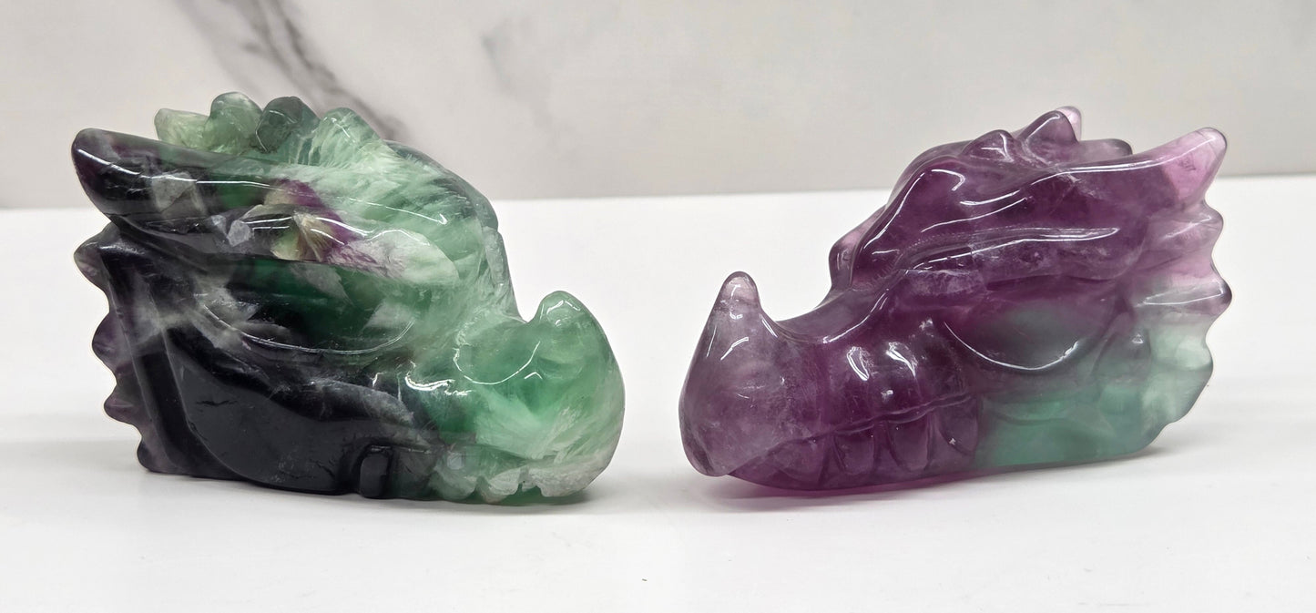 Two colorful Fluorite dragon head  carvings on a white surface