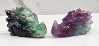 Two colorful Fluorite dragon head  carvings on a white surface