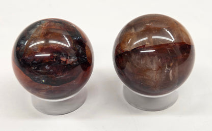 Two polished Fire Quartz spheres on clear stands against a white background