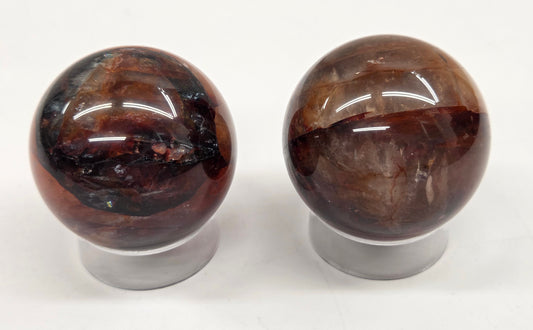 Two polished Fire Quartz spheres on clear stands against a white background