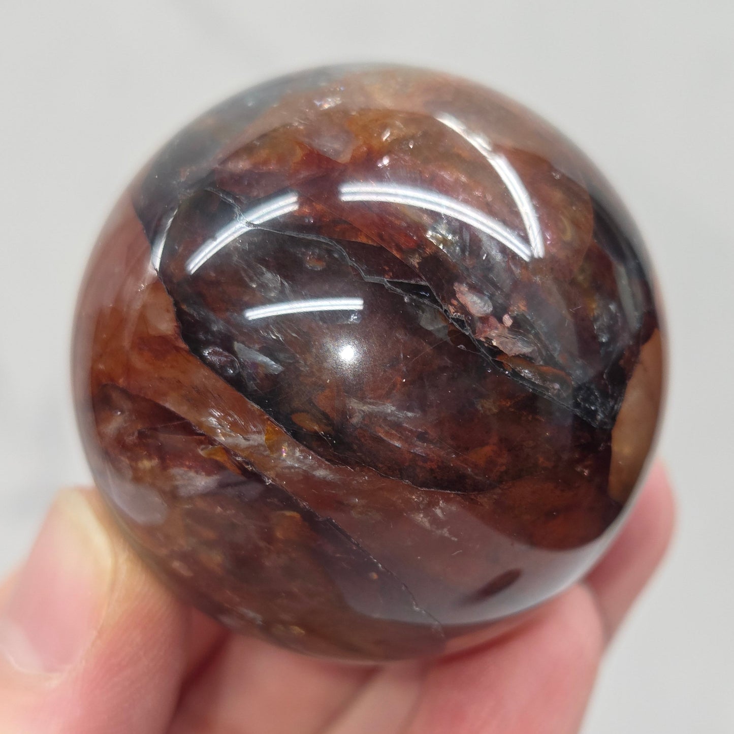Hand holding a polished Fire Quartz sphere against a plain background