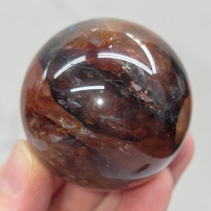 Hand holding a polished Fire Quartz sphere against a plain background