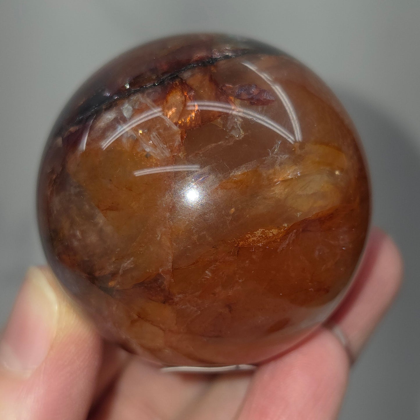 Hand holding a polished Fire Quartz sphere against a plain background
