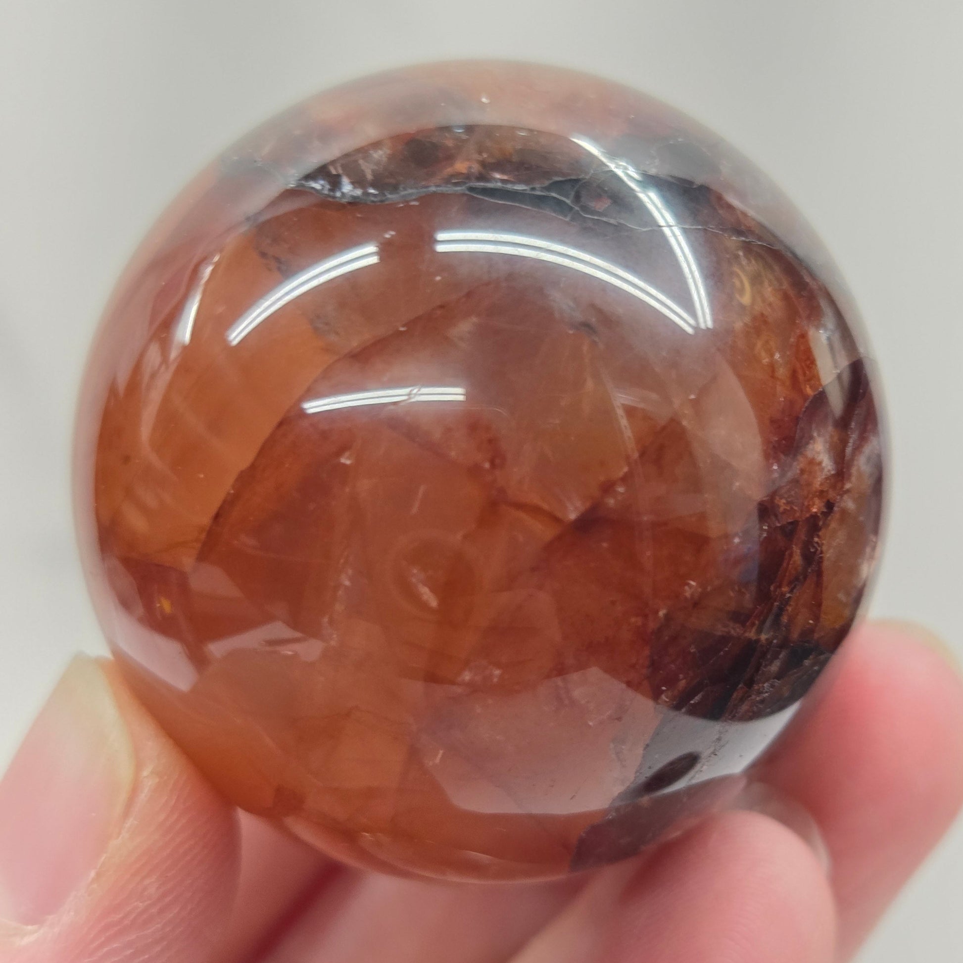 Hand holding a polished Fire Quartz sphere against a plain background