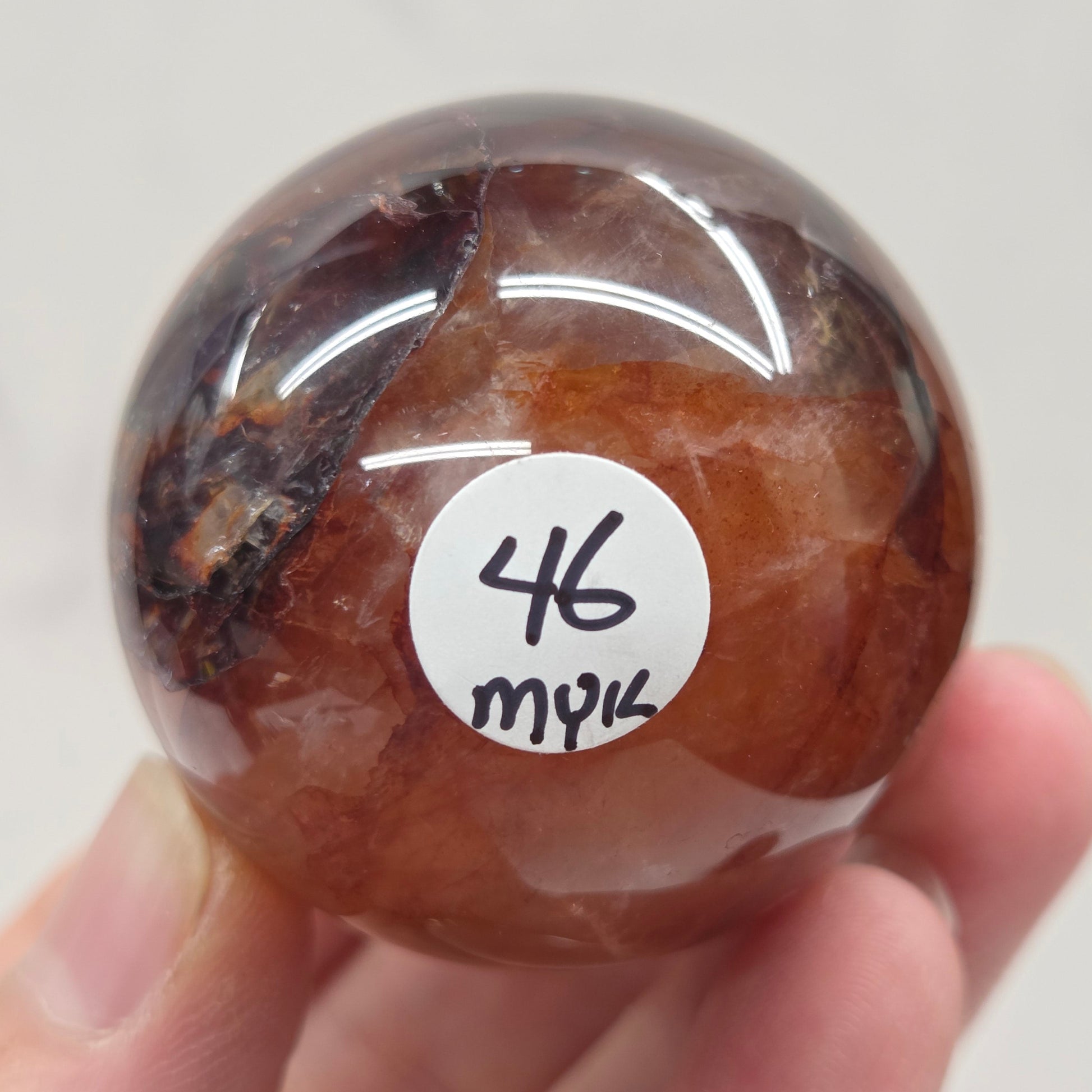 Hand holding a polished Fire Quartz sphere against a plain background