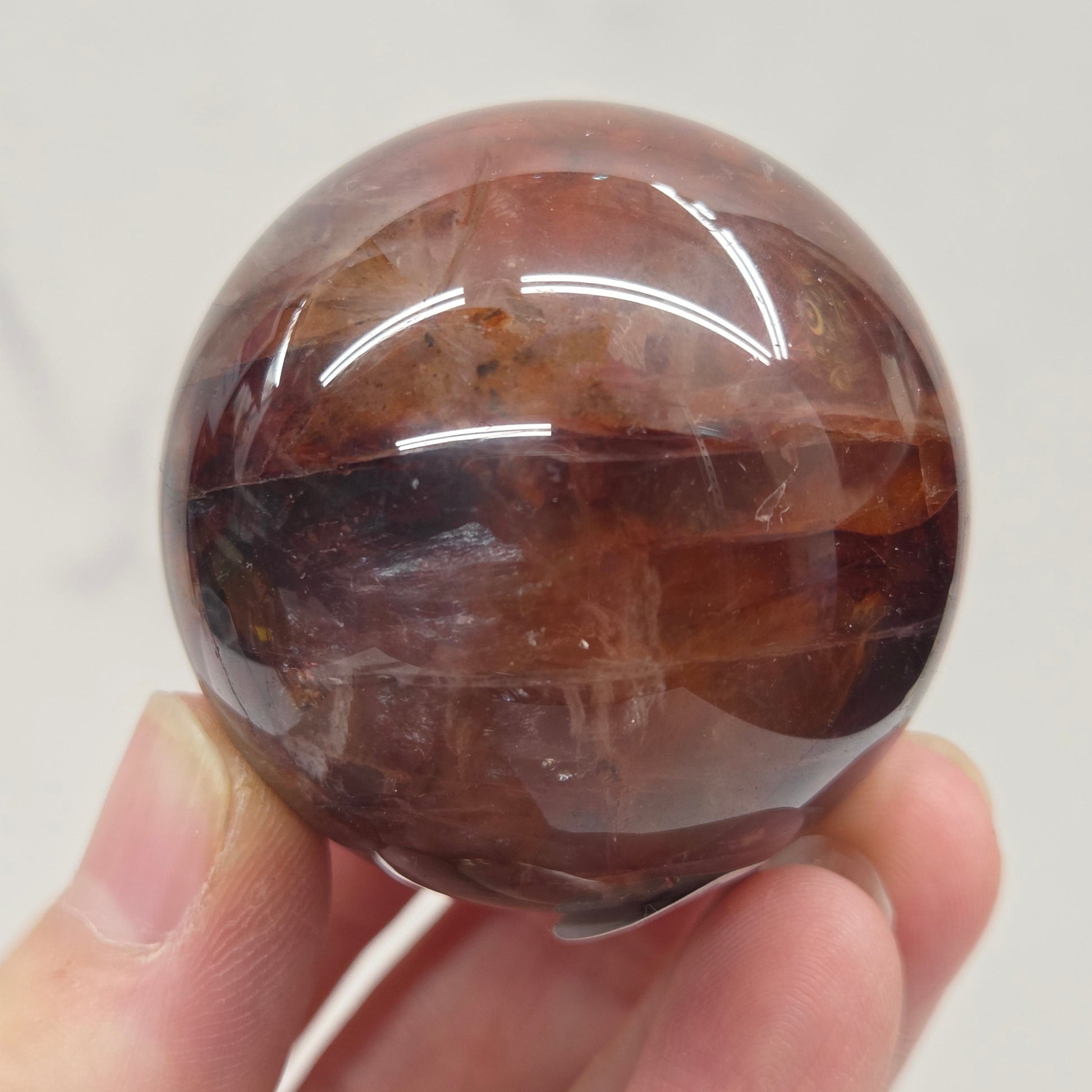 Hand holding a polished Fire Quartz sphere against a plain background
