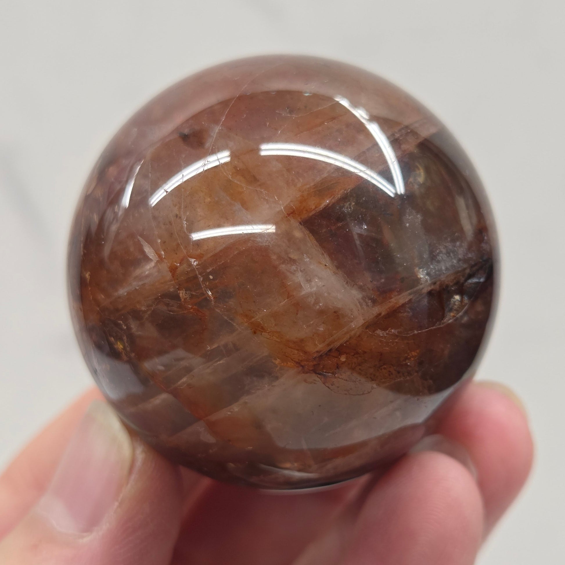 Hand holding a polished Fire Quartz sphere against a plain background