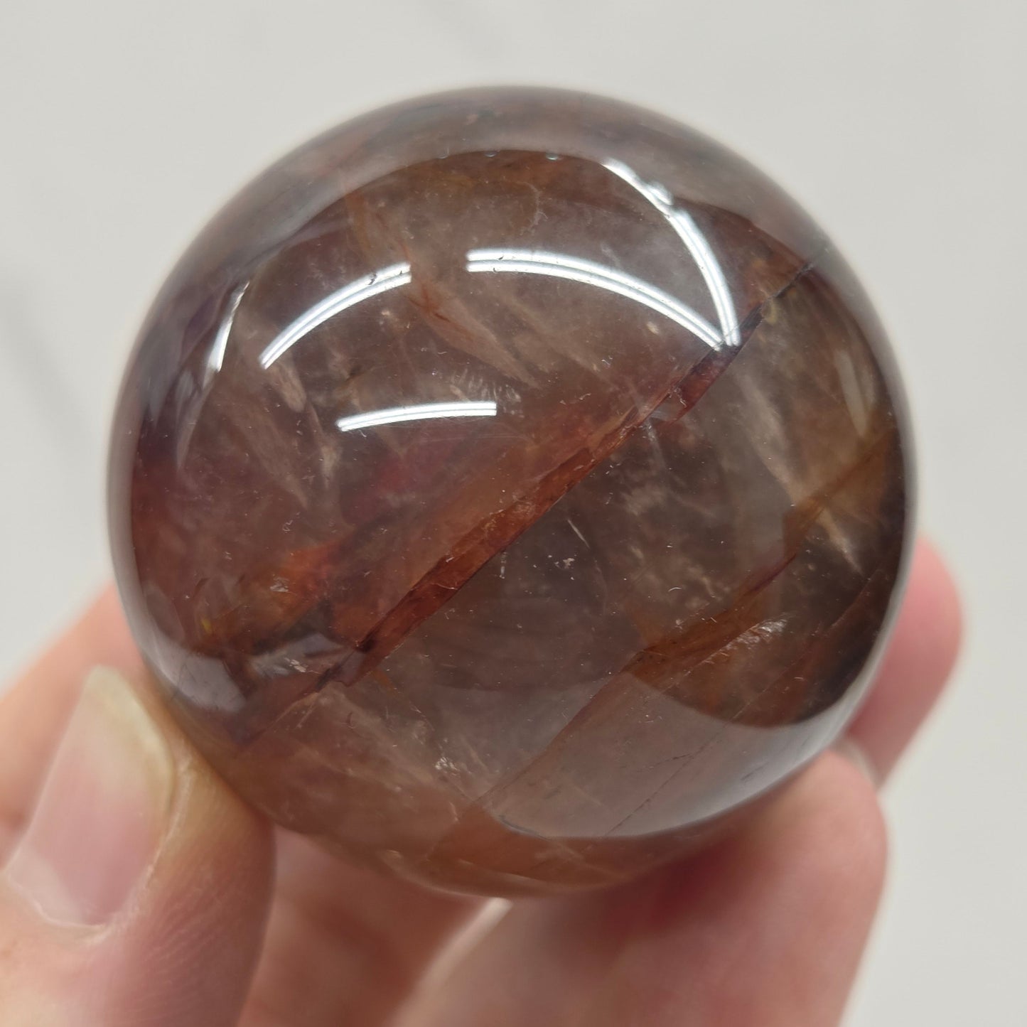 Hand holding a polished Fire Quartz sphere against a plain background