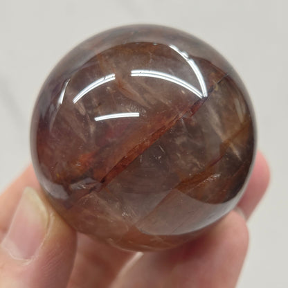 Hand holding a polished Fire Quartz sphere against a plain background
