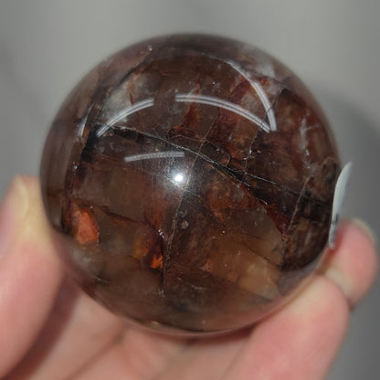 Hand holding a polished Fire Quartz sphere against a plain background
