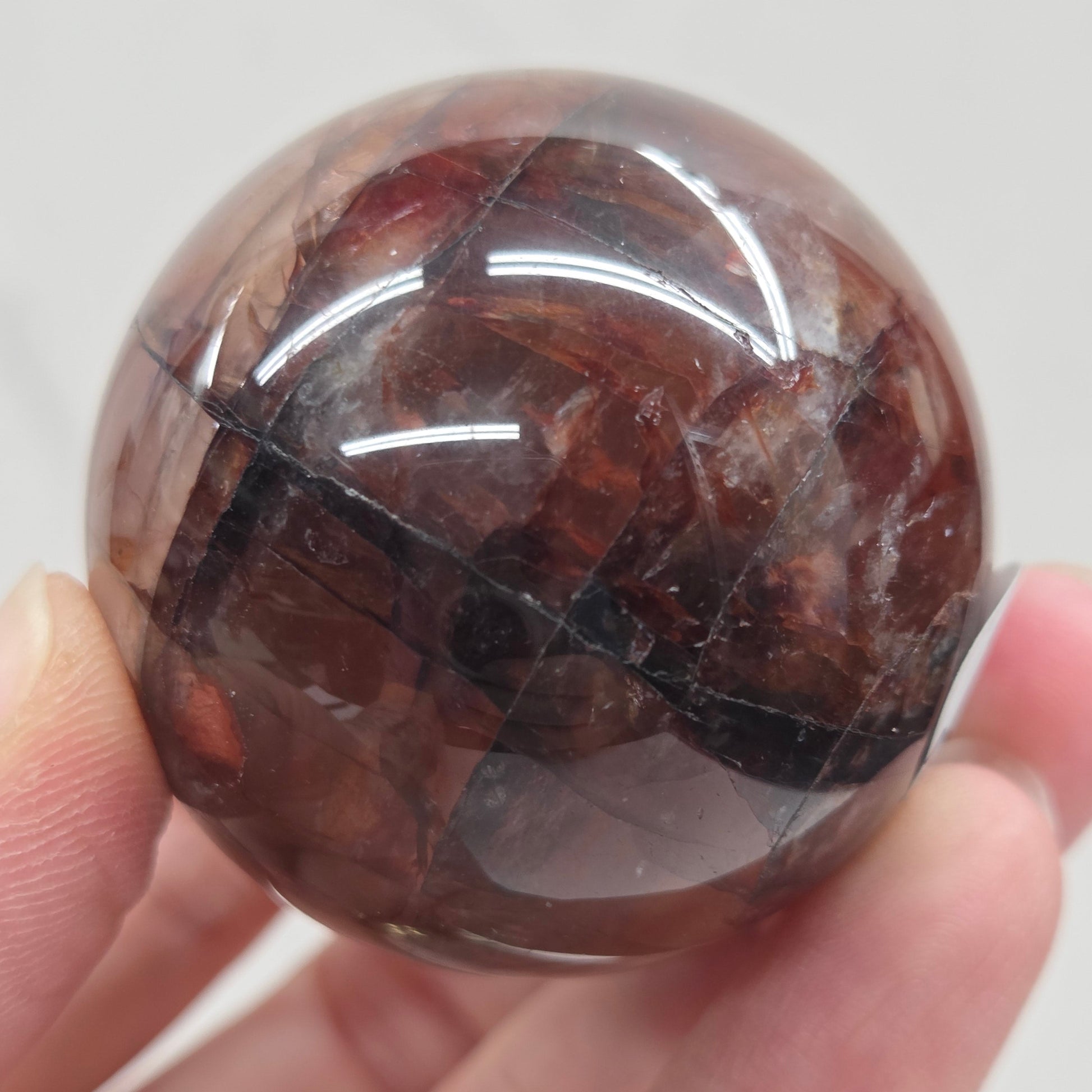 Hand holding a polished Fire Quartz sphere against a plain background