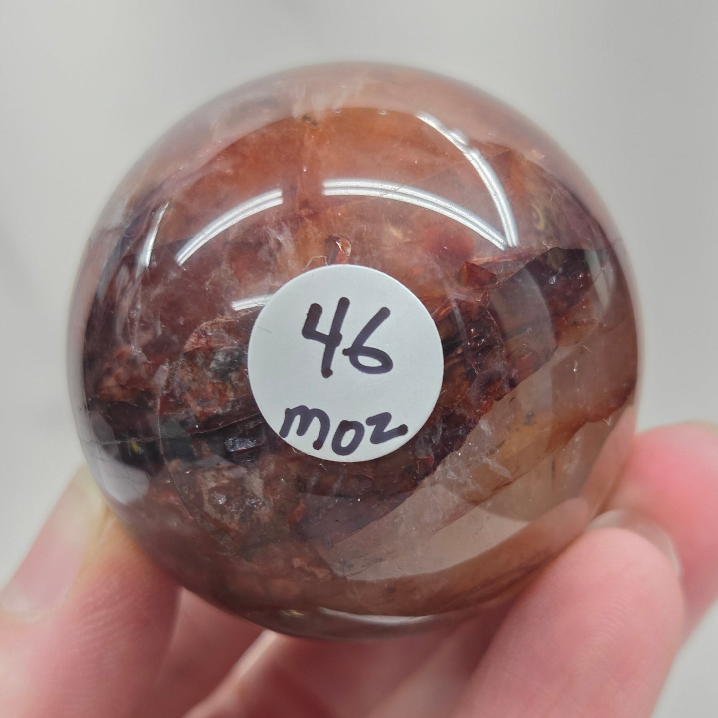 Hand holding a polished Fire Quartz sphere against a plain background