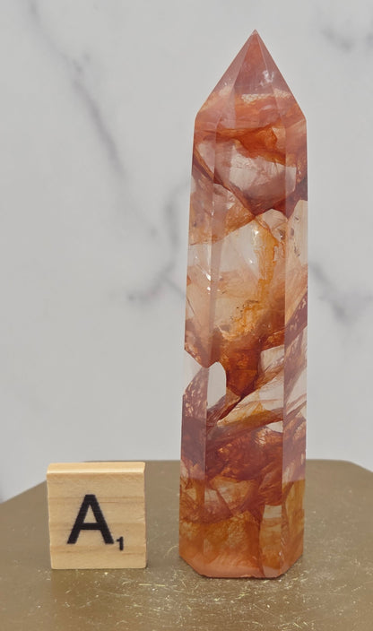 Fire Quartz crystal point with 'A1' label on a marble surface