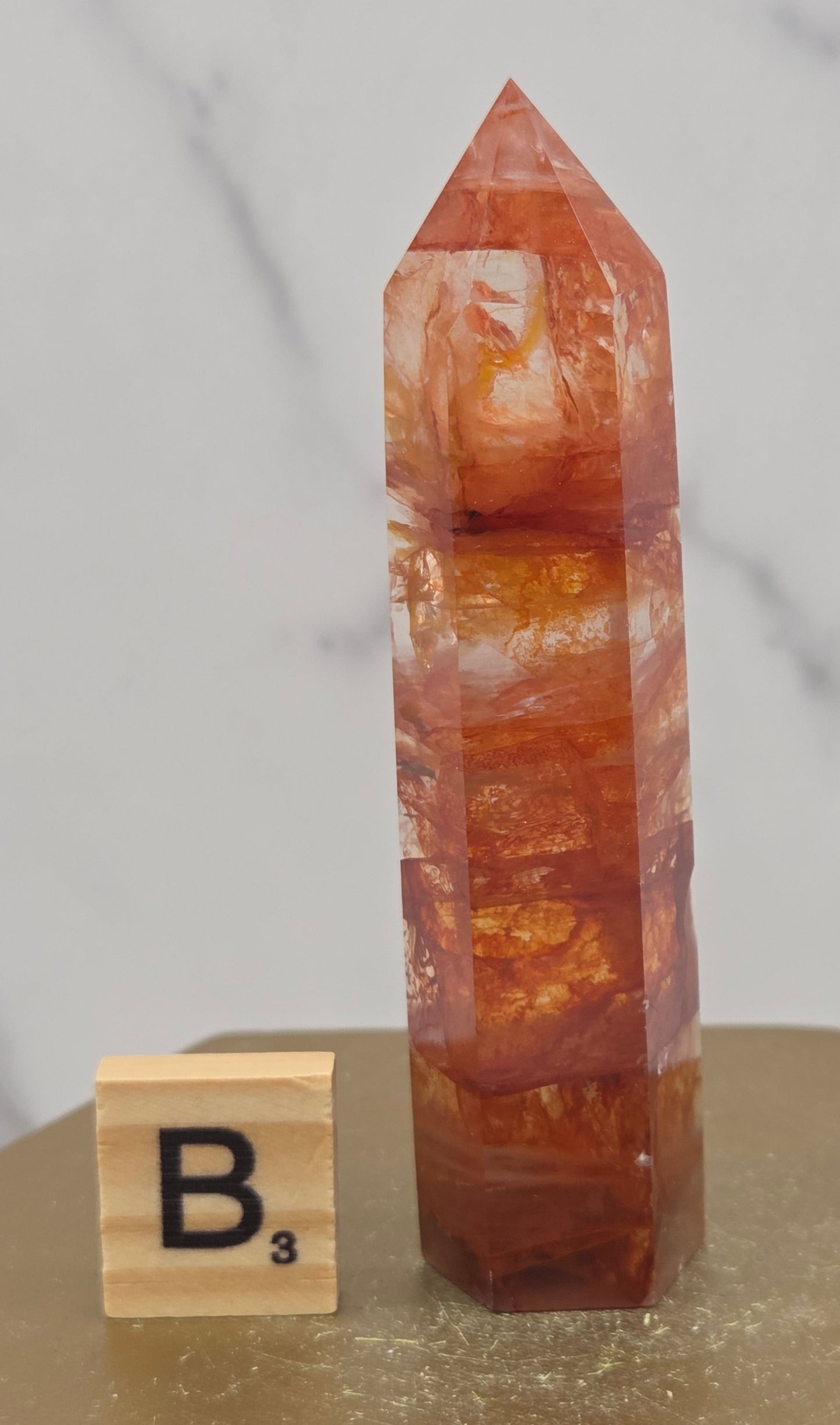 Fire Quartz crystal point with 'B3' label on a marble surface