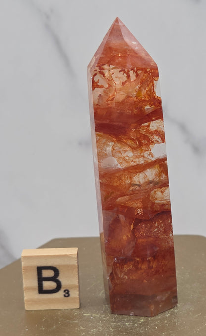 Fire Quartz crystal point with 'B3' label on a marble surface
