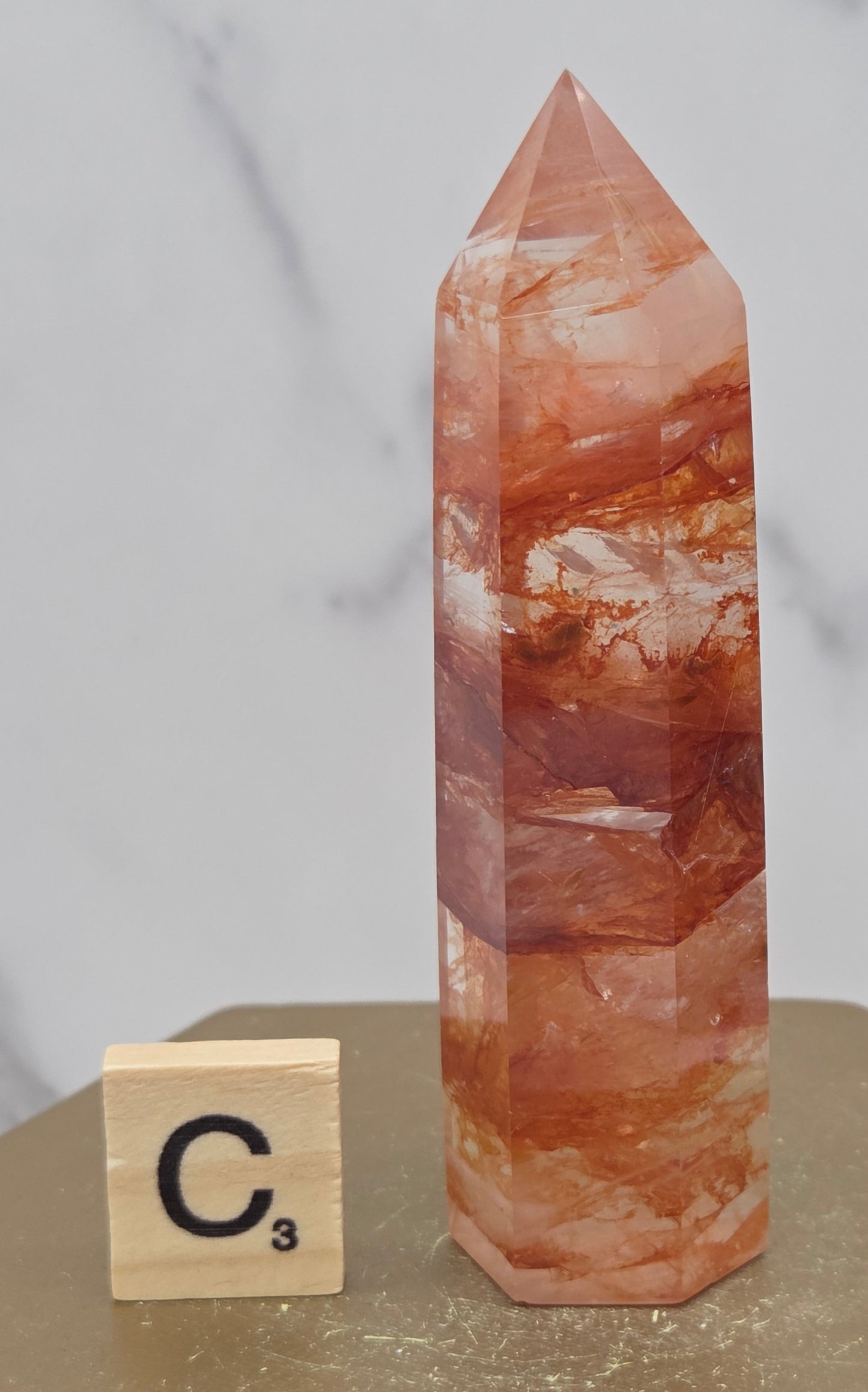 Fire Quartz crystal point with 'C3' label on a marble surface