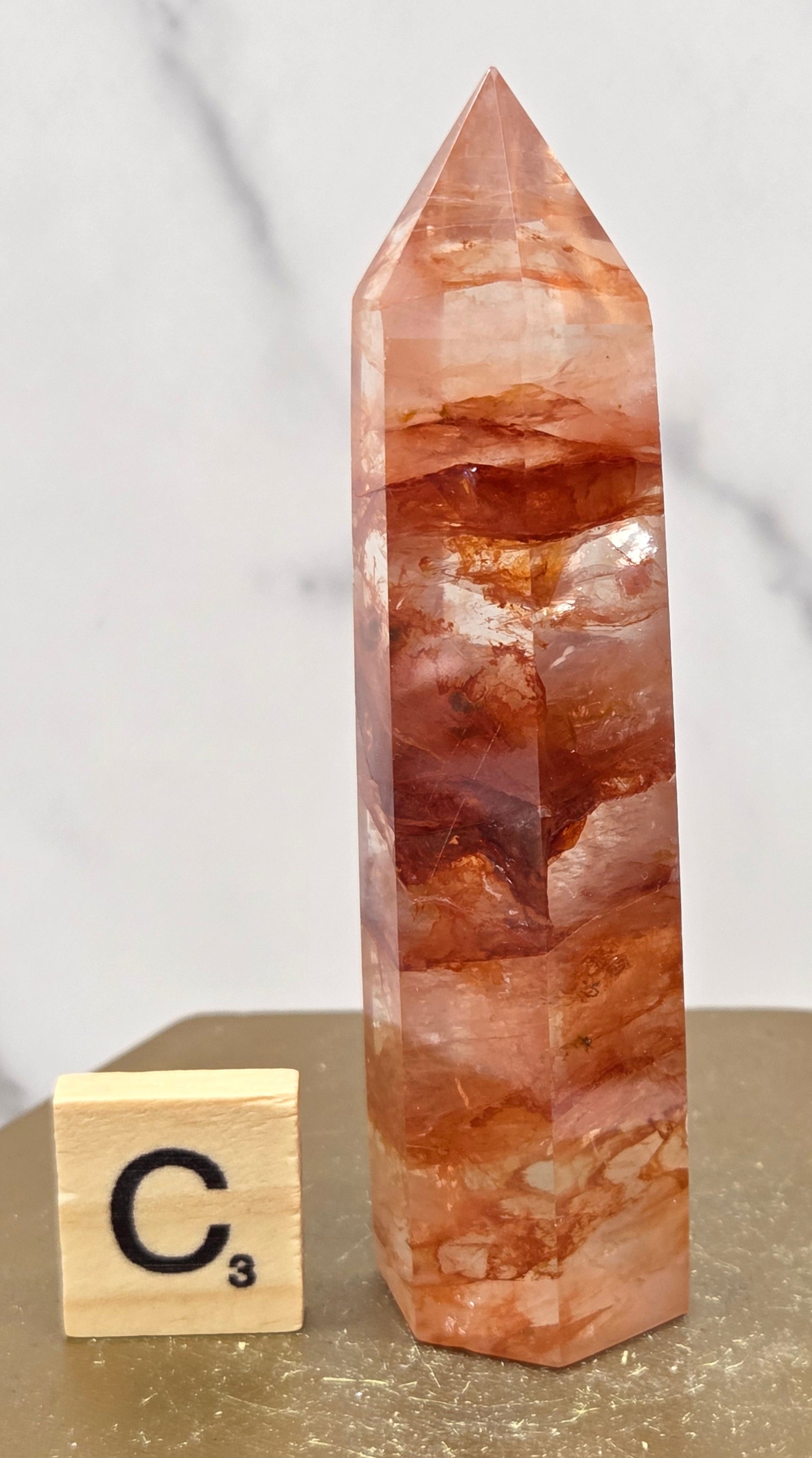 Fire Quartz crystal point with 'C3' label on a marble surface