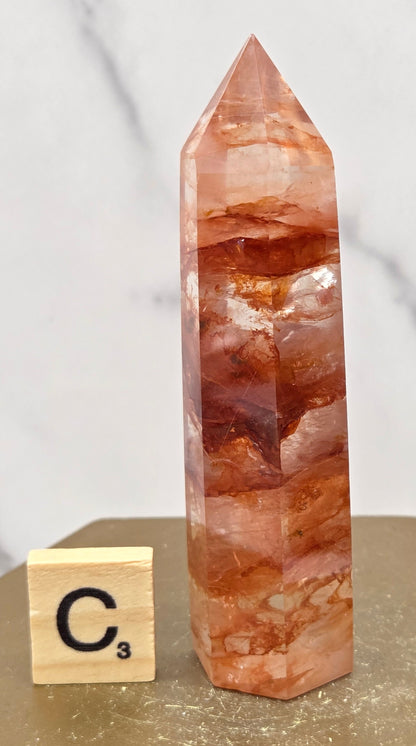 Fire Quartz crystal point with 'C3' label on a marble surface