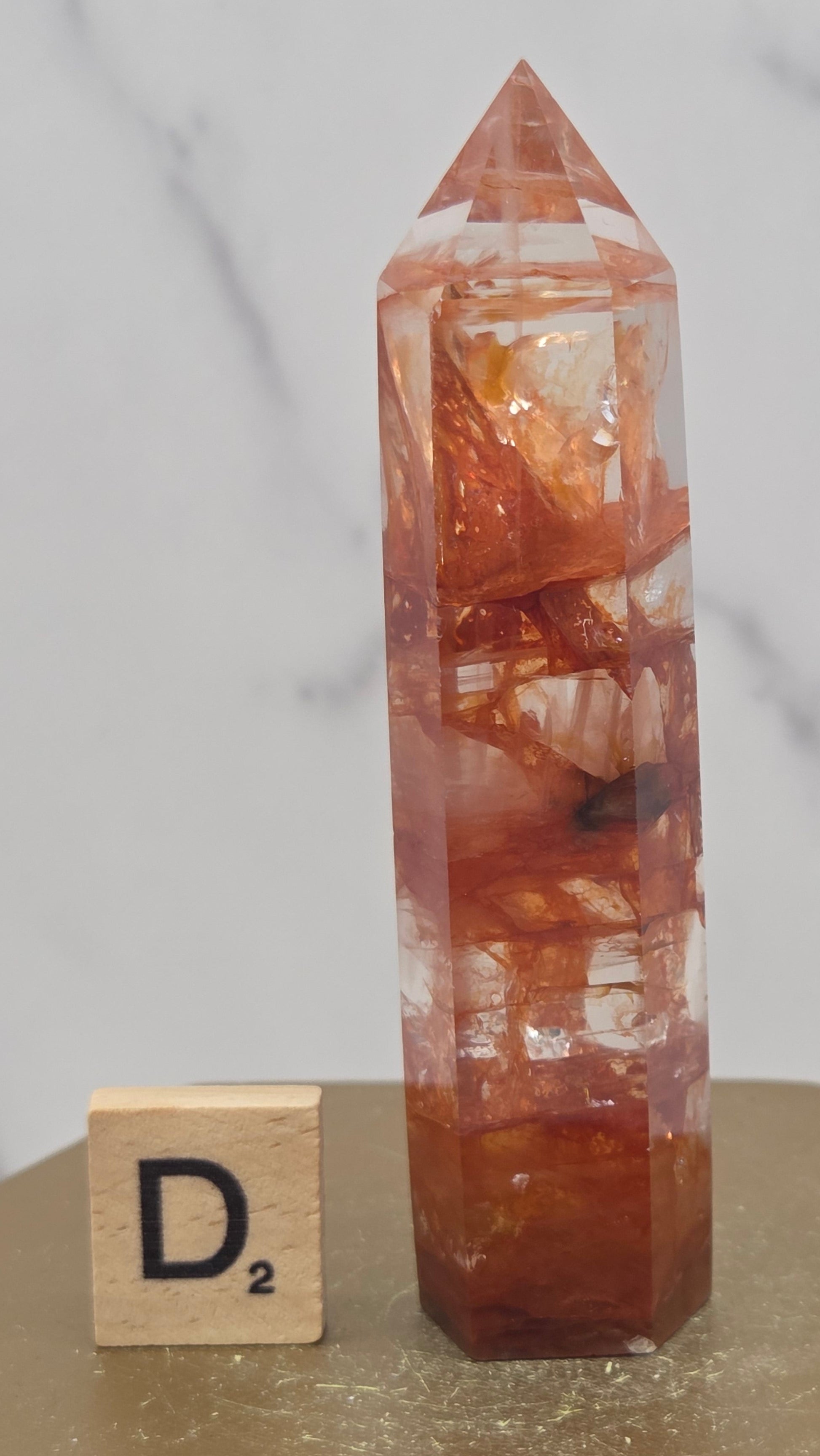 Fire Quartz crystal point with 'D2' label on a marble surface