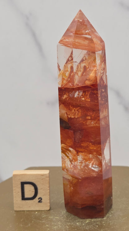 Fire Quartz crystal point with 'D2' label on a marble surface
