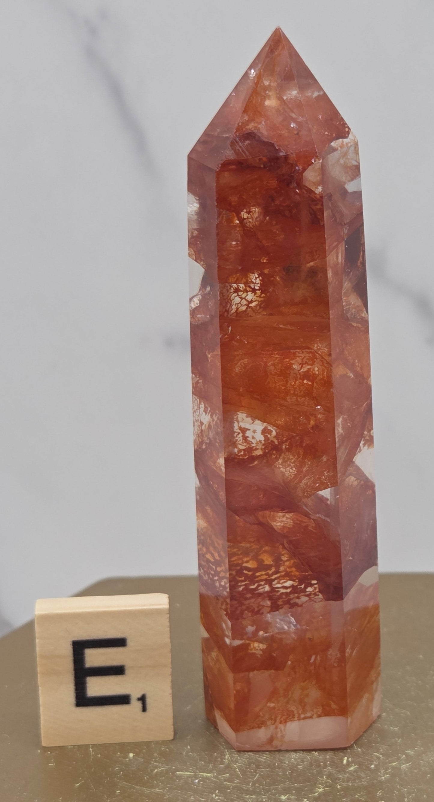 Fire Quartz crystal point with 'E1' label on a marble surface