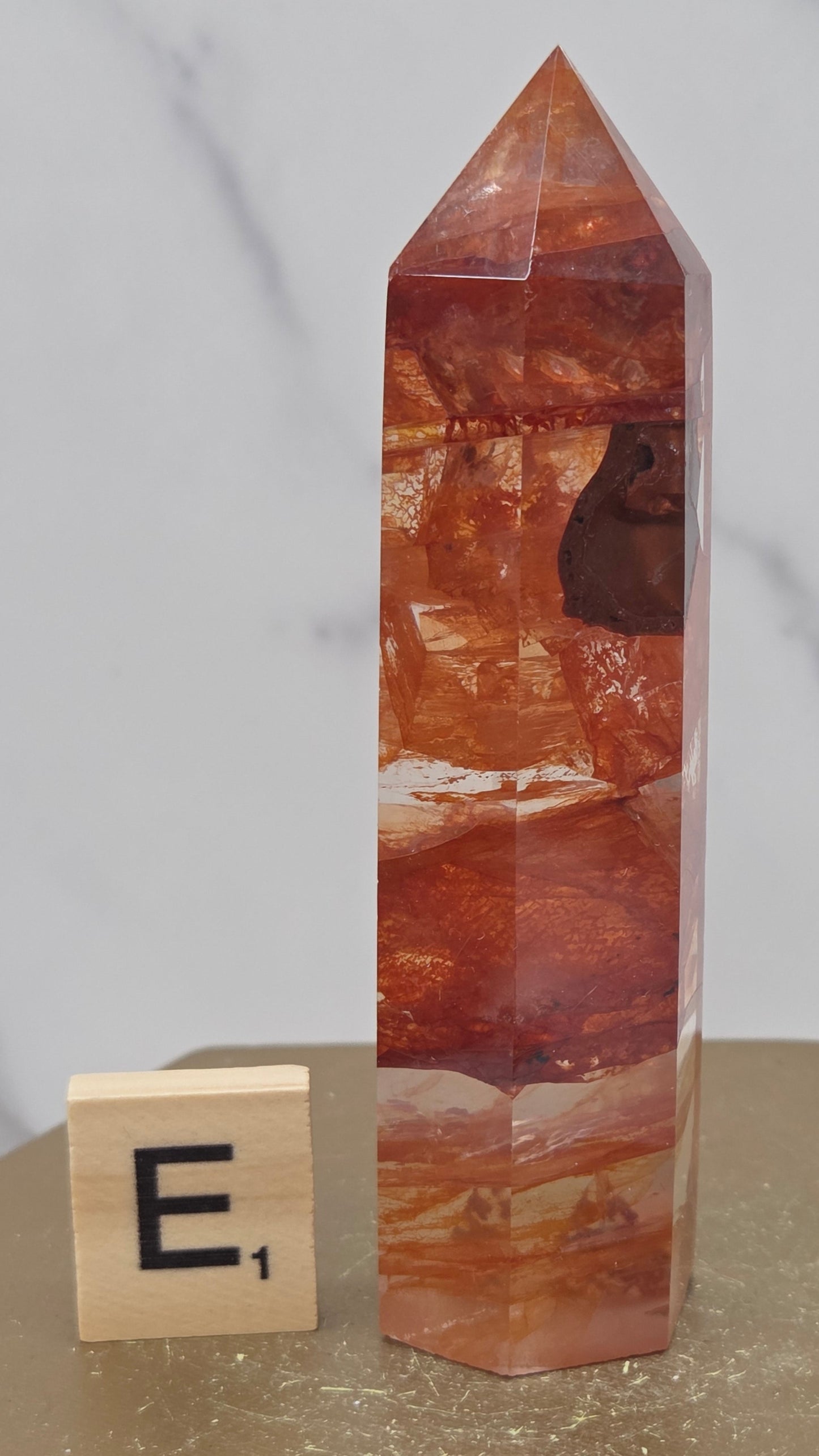Fire Quartz crystal point with 'E1' label on a marble surface