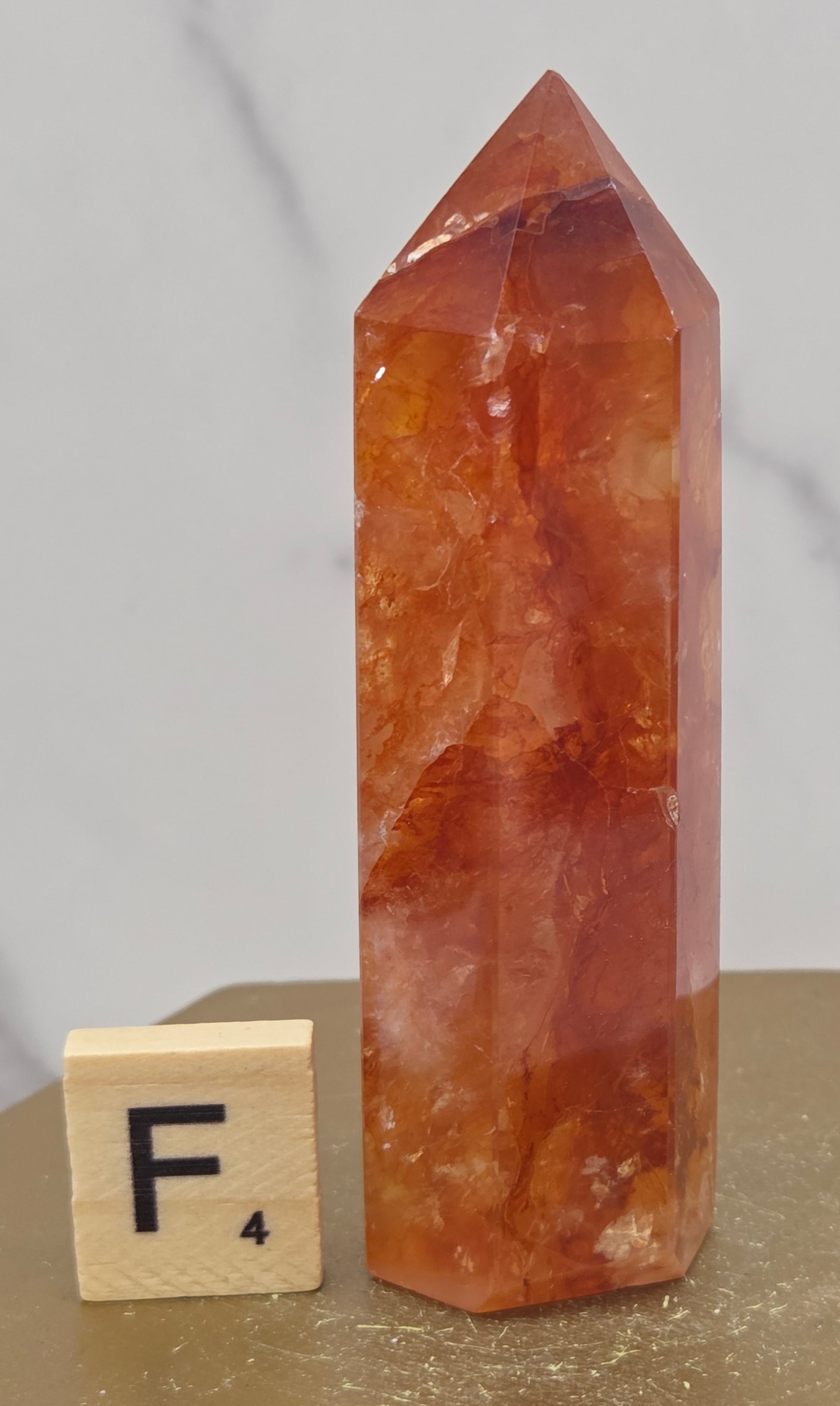Fire Quartz crystal point with 'F4' label on a marble surface