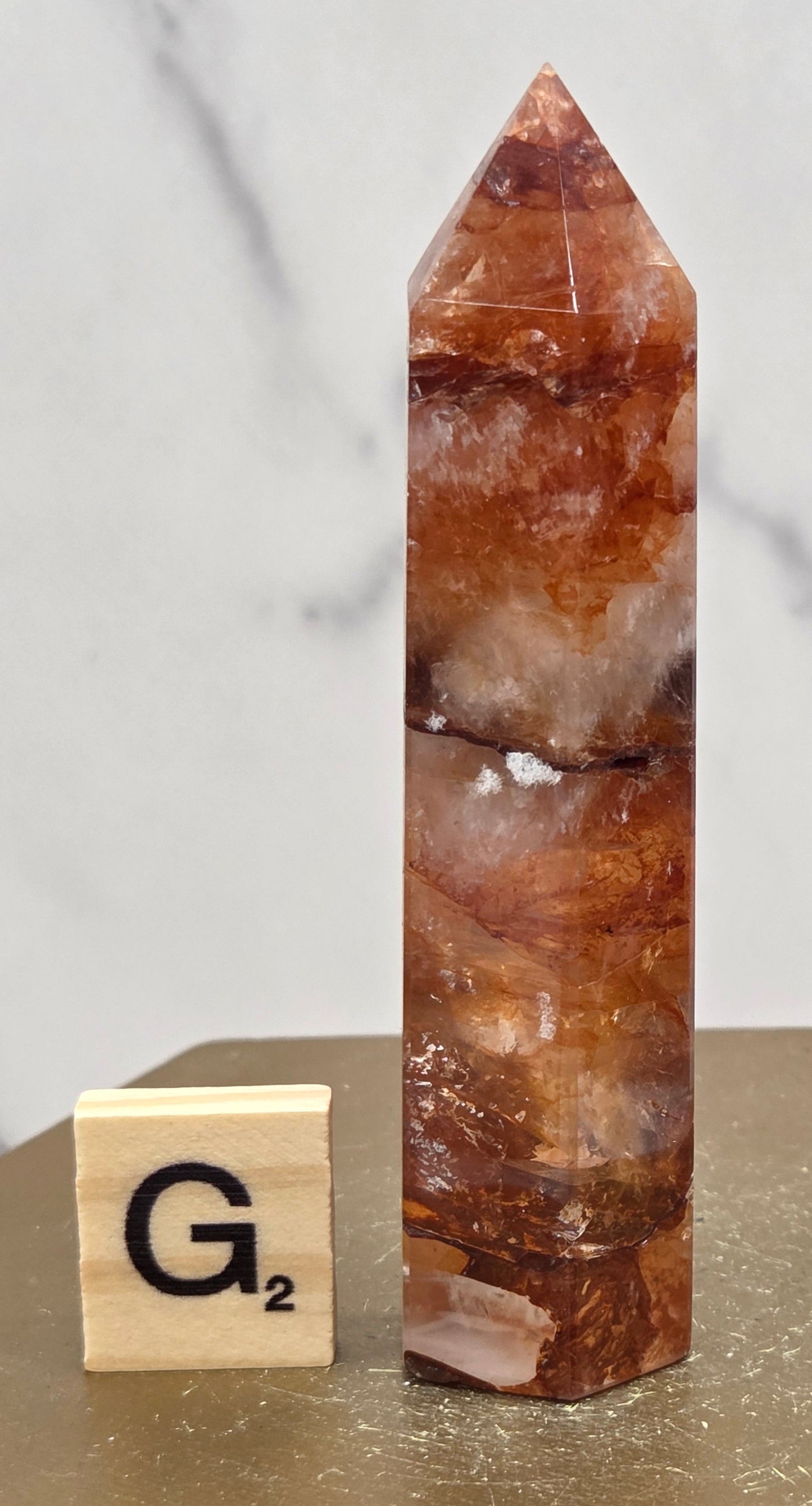 Fire Quartz crystal point with 'G2' label on a marble surface