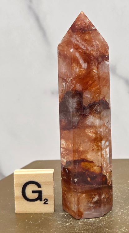 Fire Quartz crystal point with 'G2' label on a marble surface