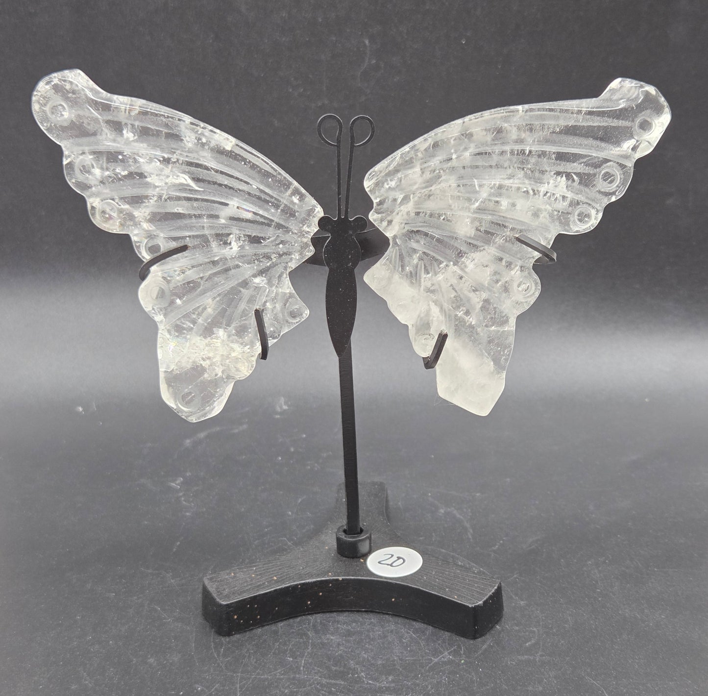 Decorative clear quartz butterfly wings on a black stand on a dark background