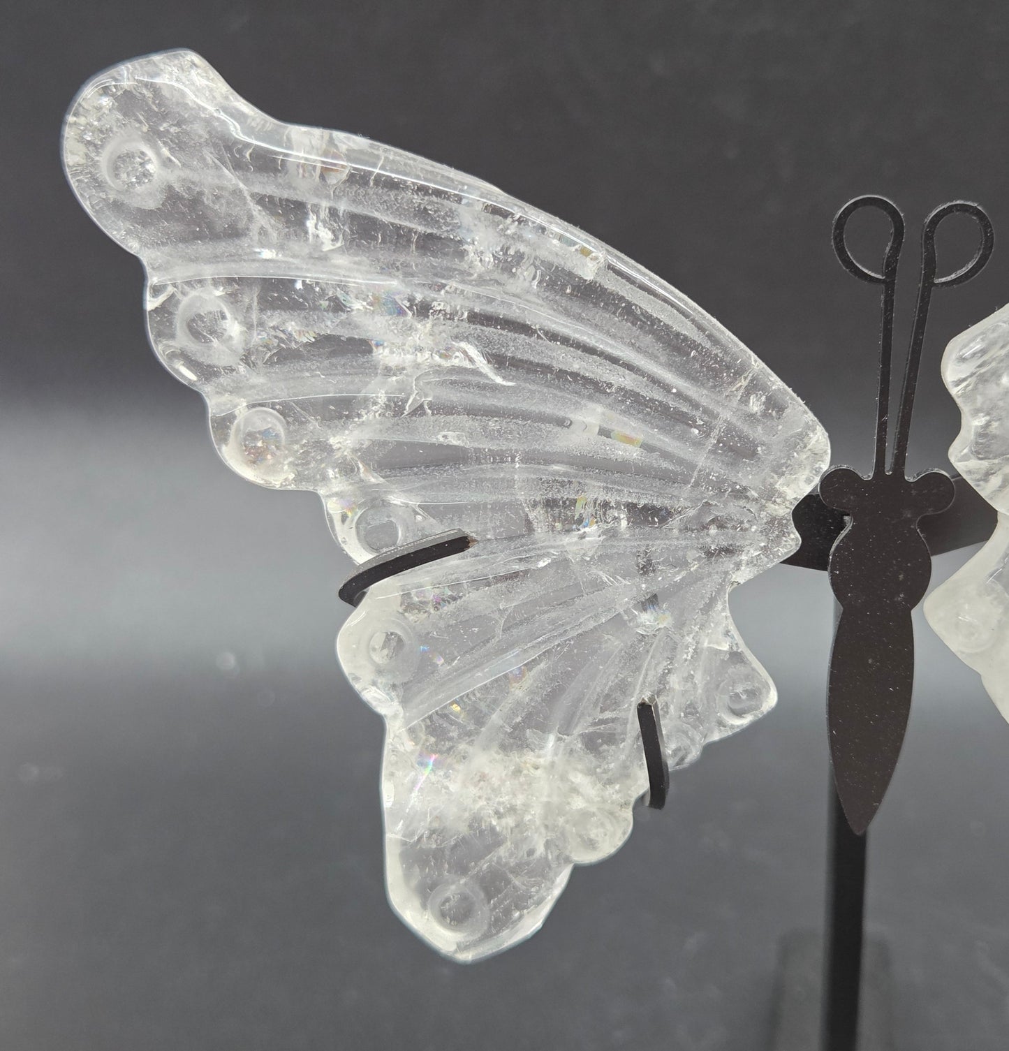 Decorative clear quartz butterfly wings on a black stand on a dark background